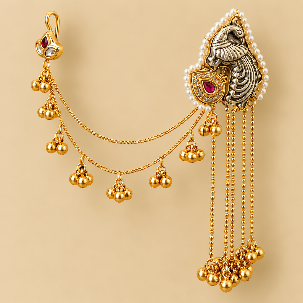 An ornate gold-toned traditional jewelry piece with dangling chains, small gold bead clusters, a pearl-bordered decorative section, and a silver-toned bird motif with red gemstone accents, shown on a plain beige background.